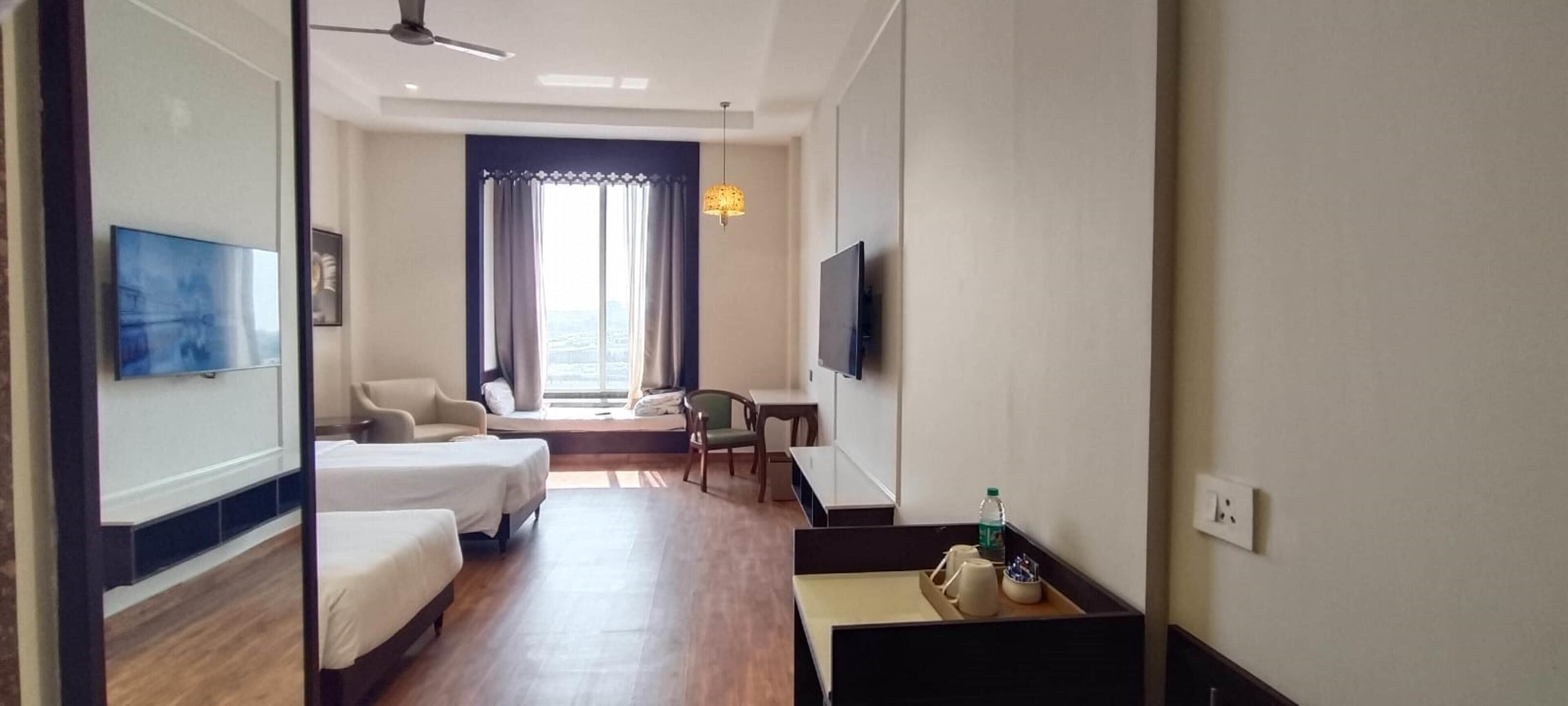 Habitación de hotel con cama, escritorio, silla, televisor y ventana con cortinas.