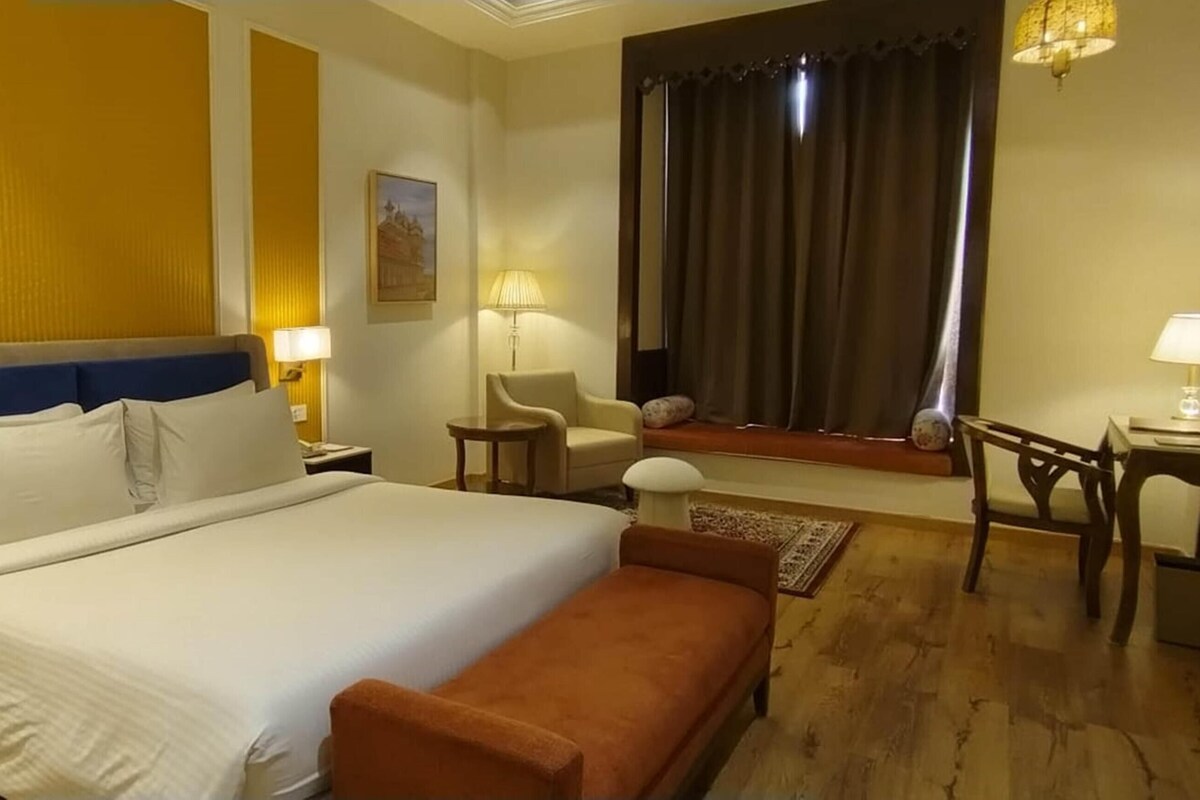 Ein Hotelzimmer mit einem Bett, Nachttischen, einem Sessel, einem kleinen Tisch und einem Spiegel.