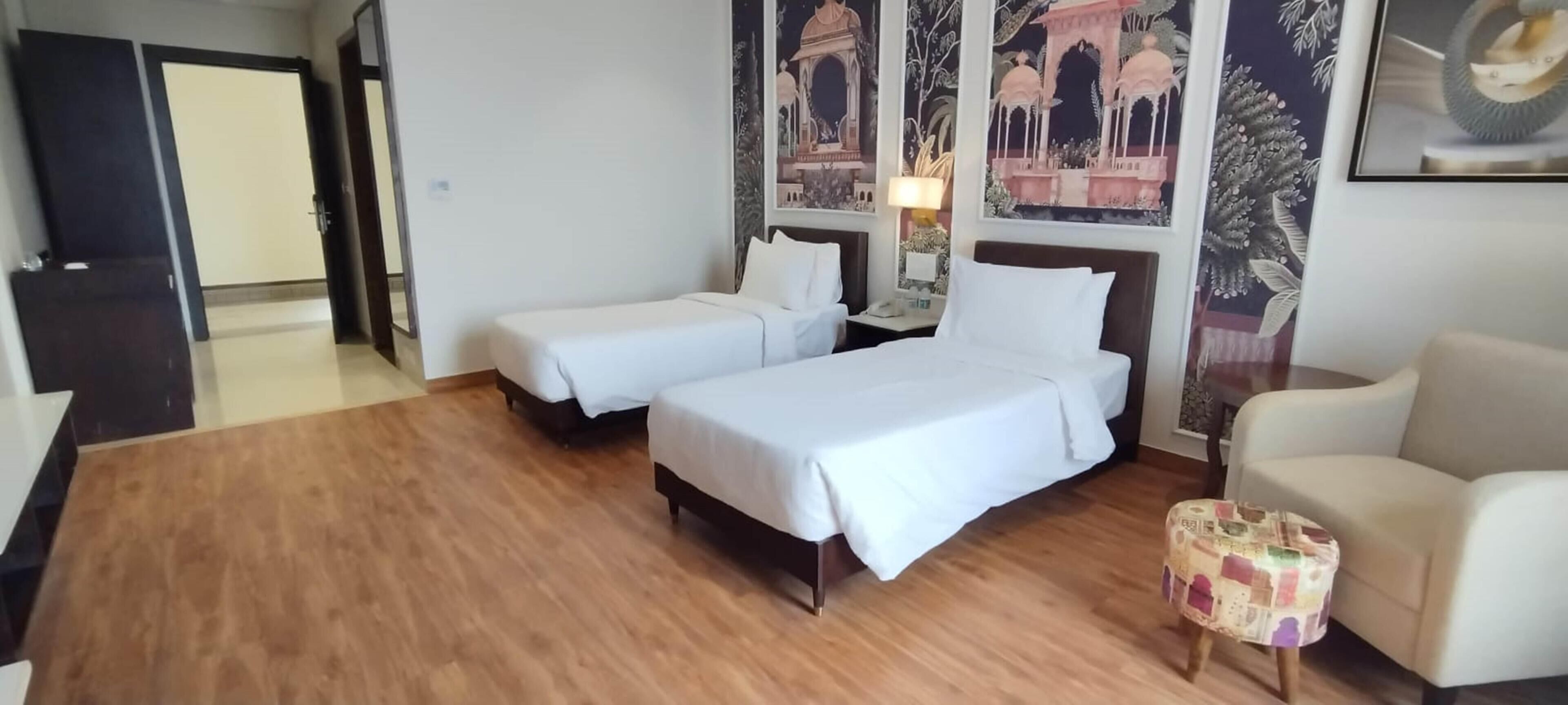 Ein Hotelzimmer mit zwei Einzelbetten, einem kleinen runden Tisch, einer Couch und einer Tür zu einem weiteren Raum.
