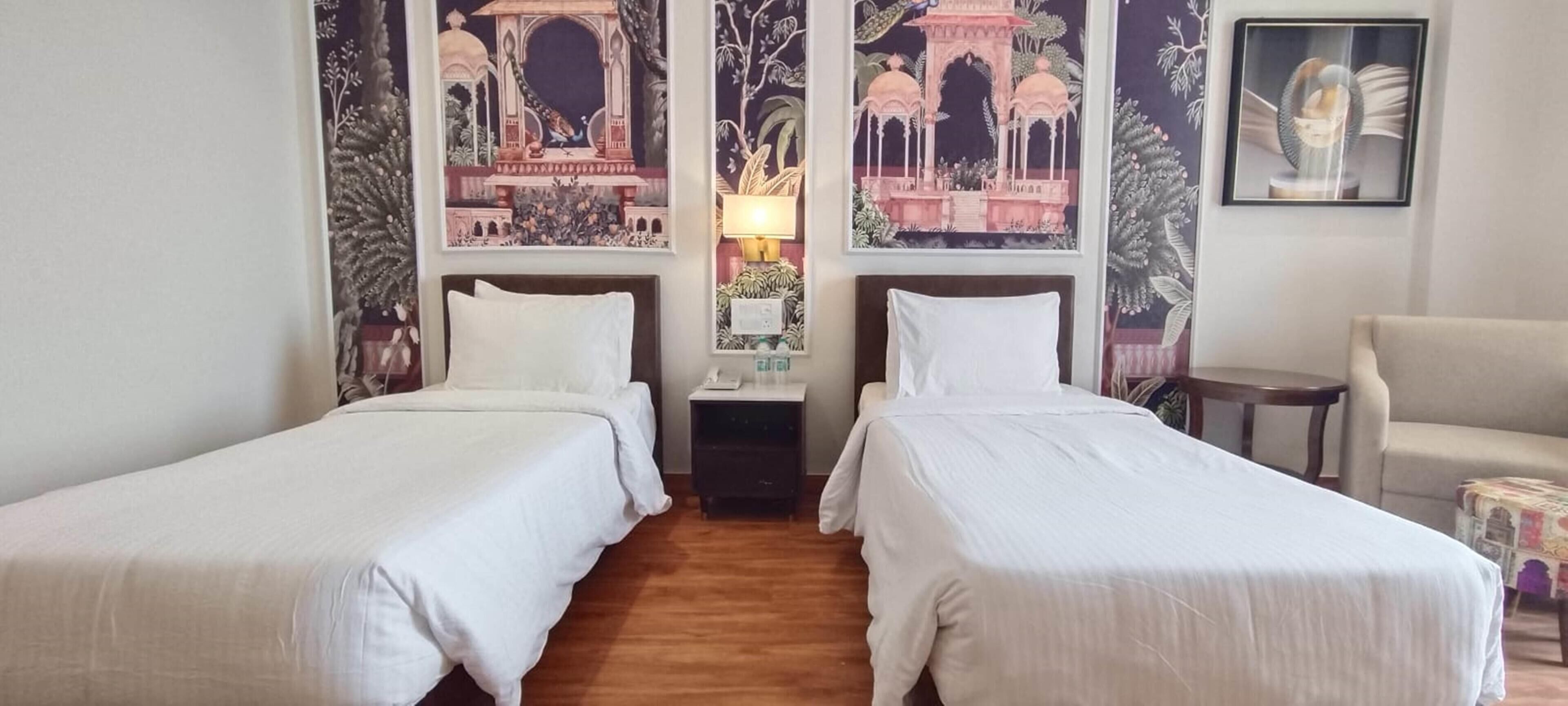 A hotel room with two single beds, a nightstand, a lamp, and a chair.