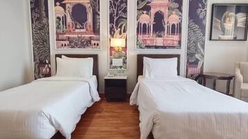 Habitación de hotel con dos camas individuales, una mesita de noche, una lámpara y una silla.