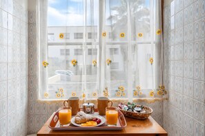 Ein Frühstücksbrett mit einem Croissant, Erdbeeren, Orangenscheiben und Orangensaft auf einem Holztisch neben einem Fenster mit sonnendurchflutetem Ausblick.