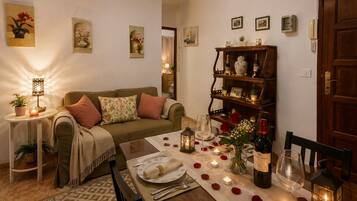 Een gezellige woonkamer met een bank, een eettafel gedekt voor twee personen en een boekenkast.