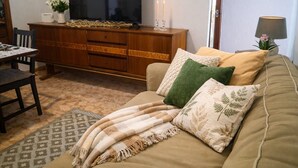 Ein Wohnzimmer mit einer Couch, einem Fernseher, einer Holzkommode, einem Tisch und einer Lampe.