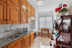Cozinha com armários de madeira, micro-ondas, pia e janela com cortinas.