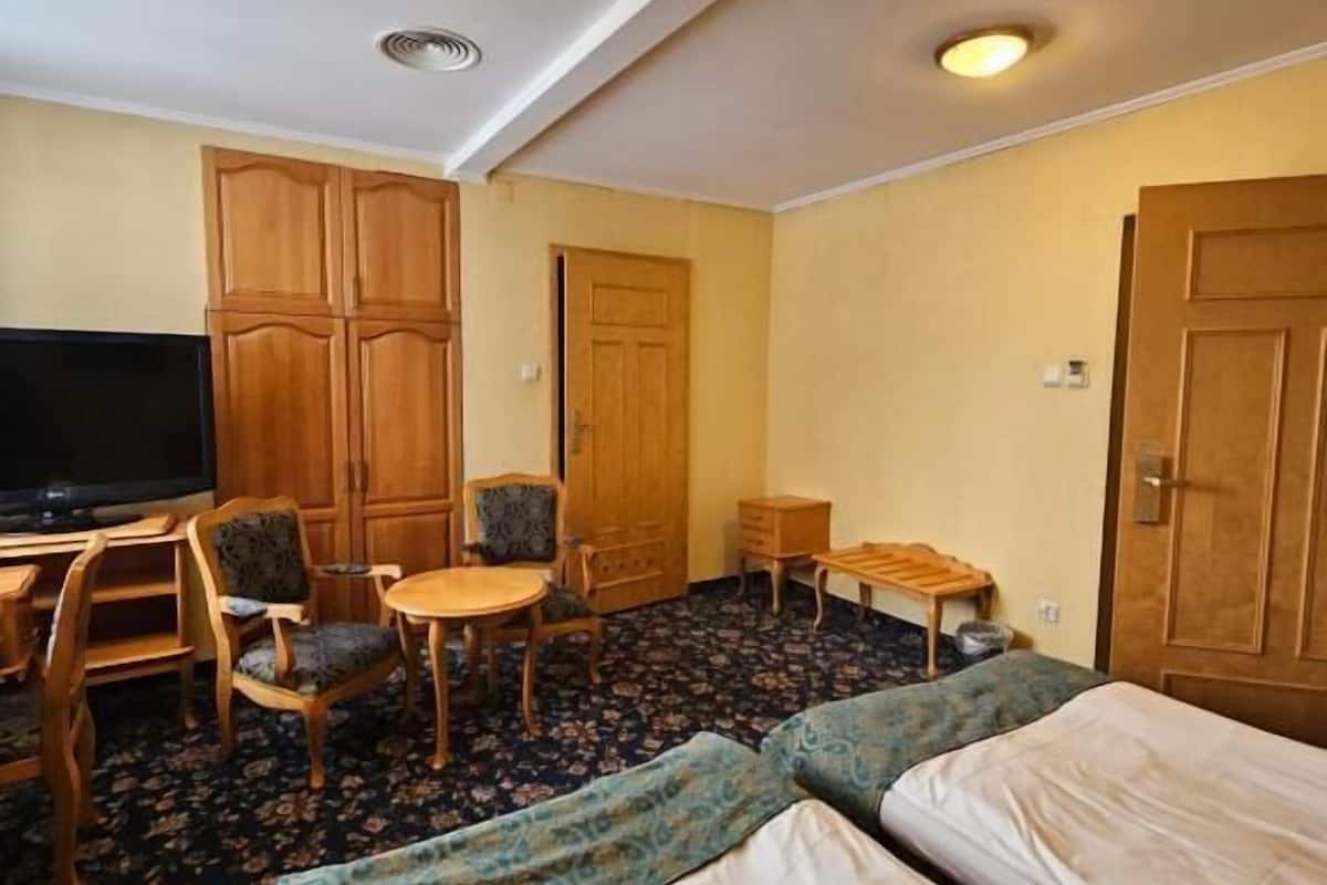 A hotel room with two beds, a desk, a chair, a TV, and wooden wardrobes.