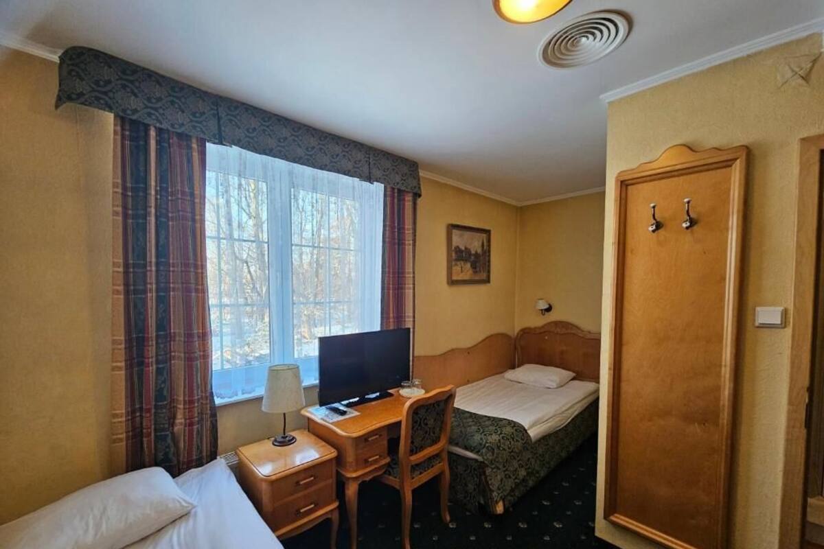 A hotel room with a bed, a desk with a computer, a chair, a wardrobe, and a window with curtains.