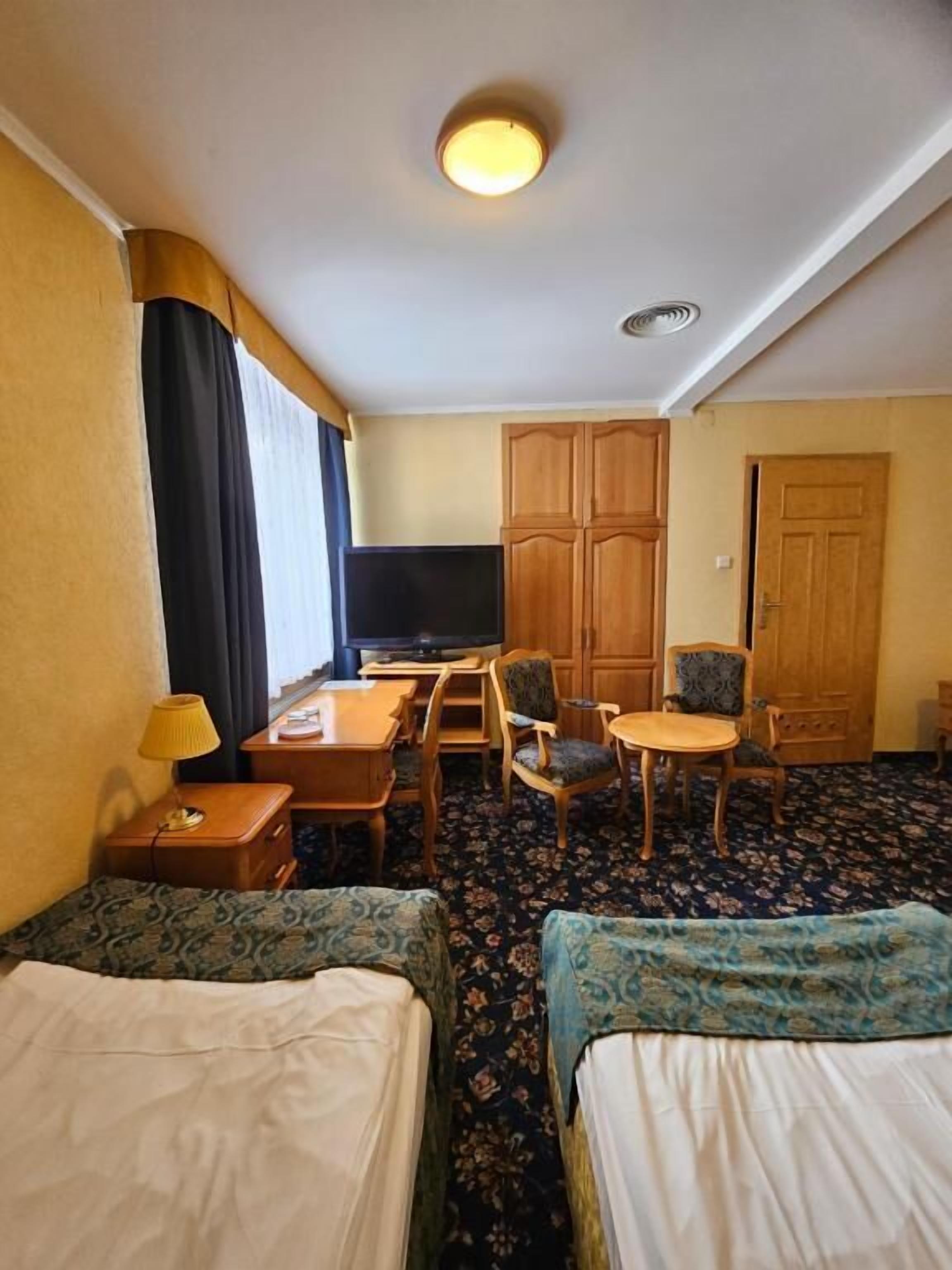 A hotel room with two beds, a desk, a TV, a wardrobe, and a door.