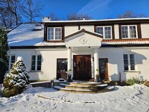 A two-story house with a central entrance, a snow-covered roof, and a small tree in the foreground. - Folwark Historic Hotel (Warsaw)