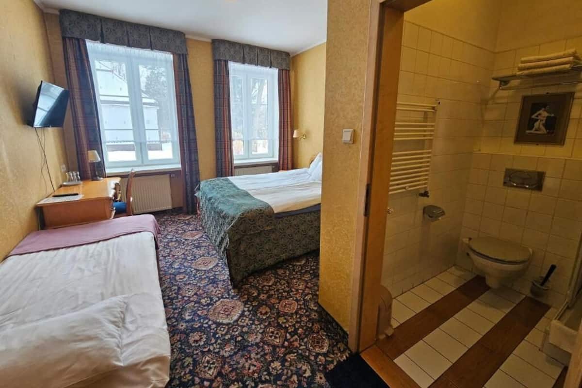 A hotel room with two beds, a bathroom with a toilet and shower, and a small desk with a chair.
