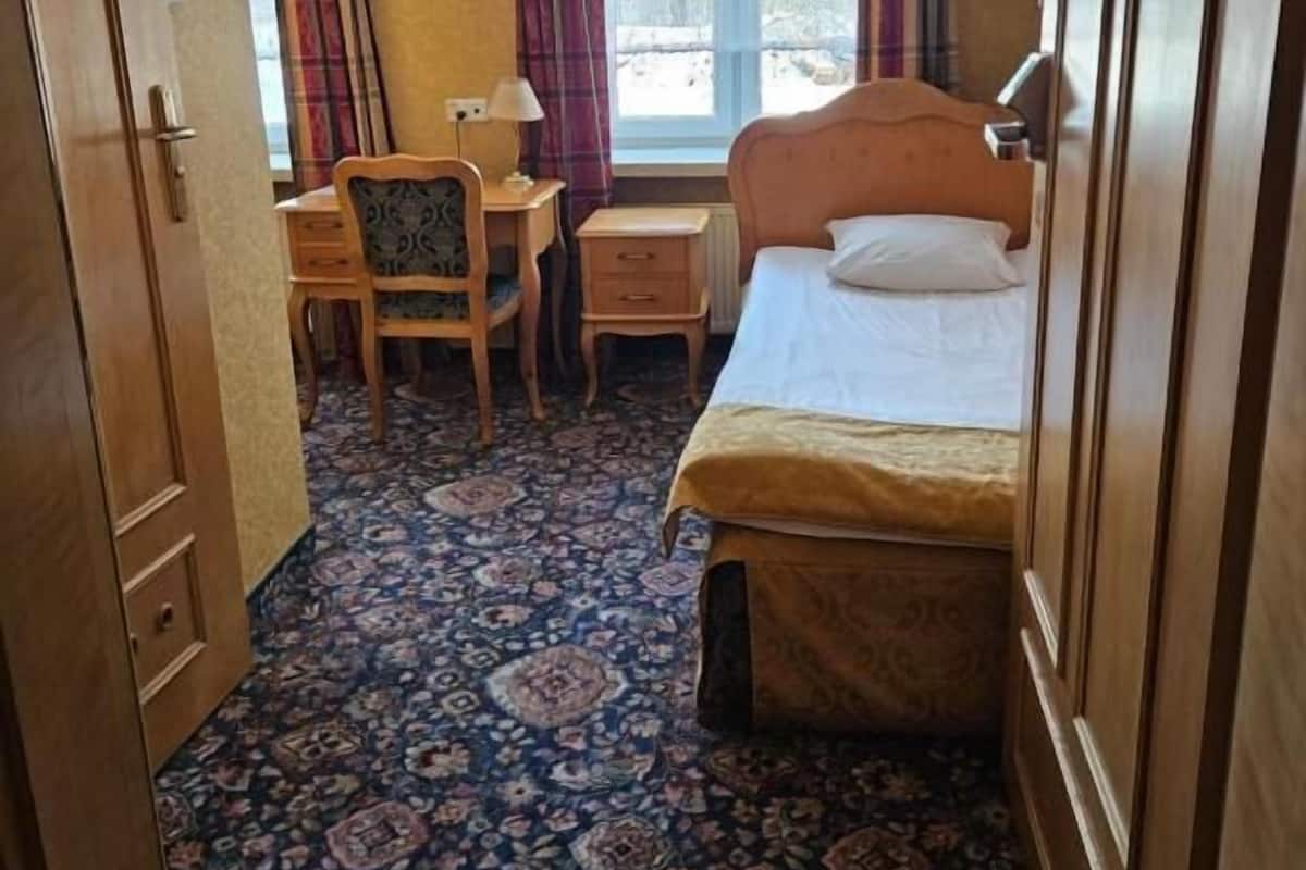 A hotel room with a bed, a desk, a chair, and a window with curtains.