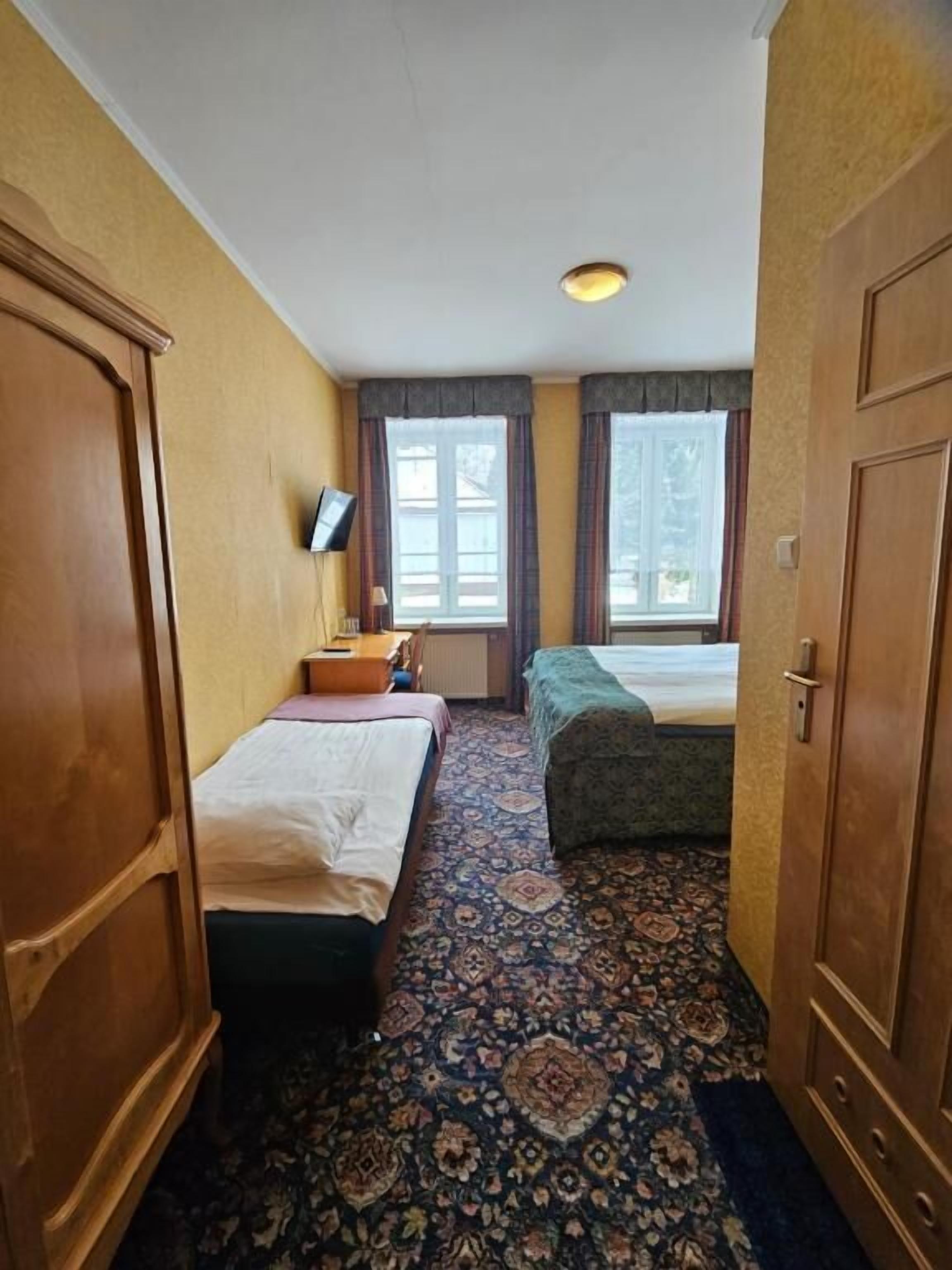 Ein Hotelzimmer mit zwei Betten, einem Schreibtisch, einem Sessel, einem Fernseher und einem Fenster mit Vorhängen.