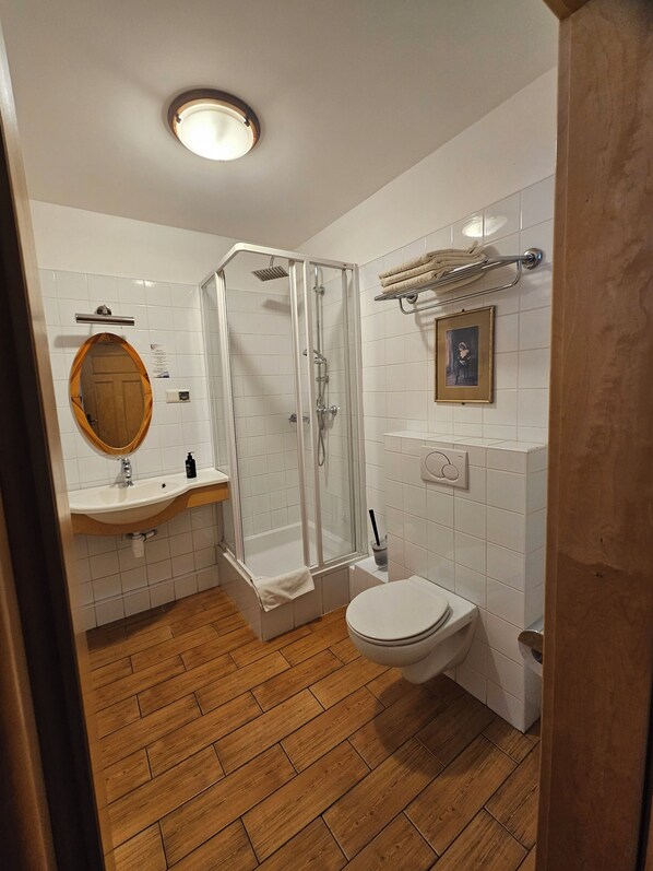 A bathroom with a wooden floor, a glass-enclosed shower, a white sink, a toilet, and a towel rack. - Folwark Historic Hotel (Warsaw)
