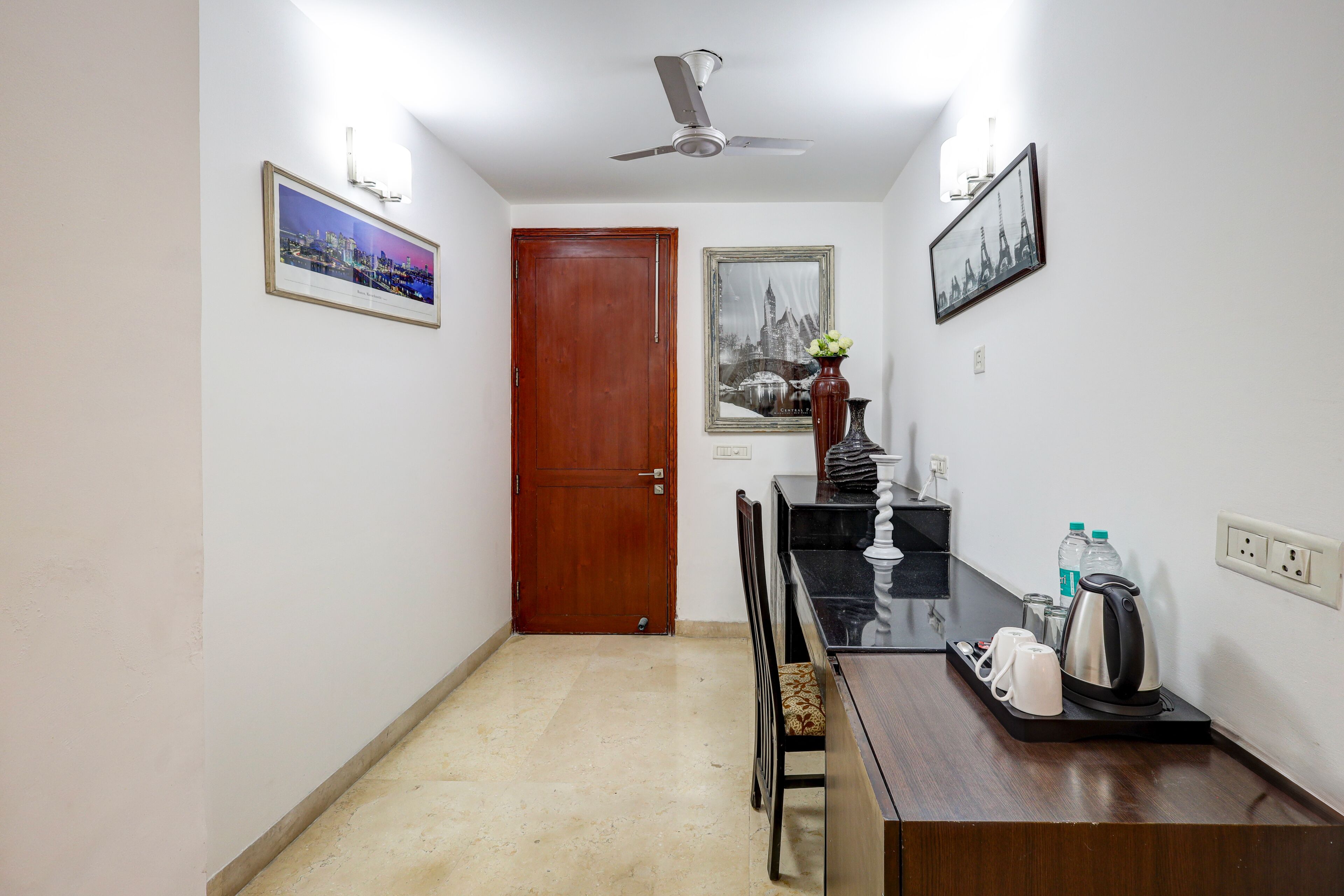Habitación de hotel con puerta de madera, una mesa de comedor con sillas, una cafetera y dos cuadros en la pared.