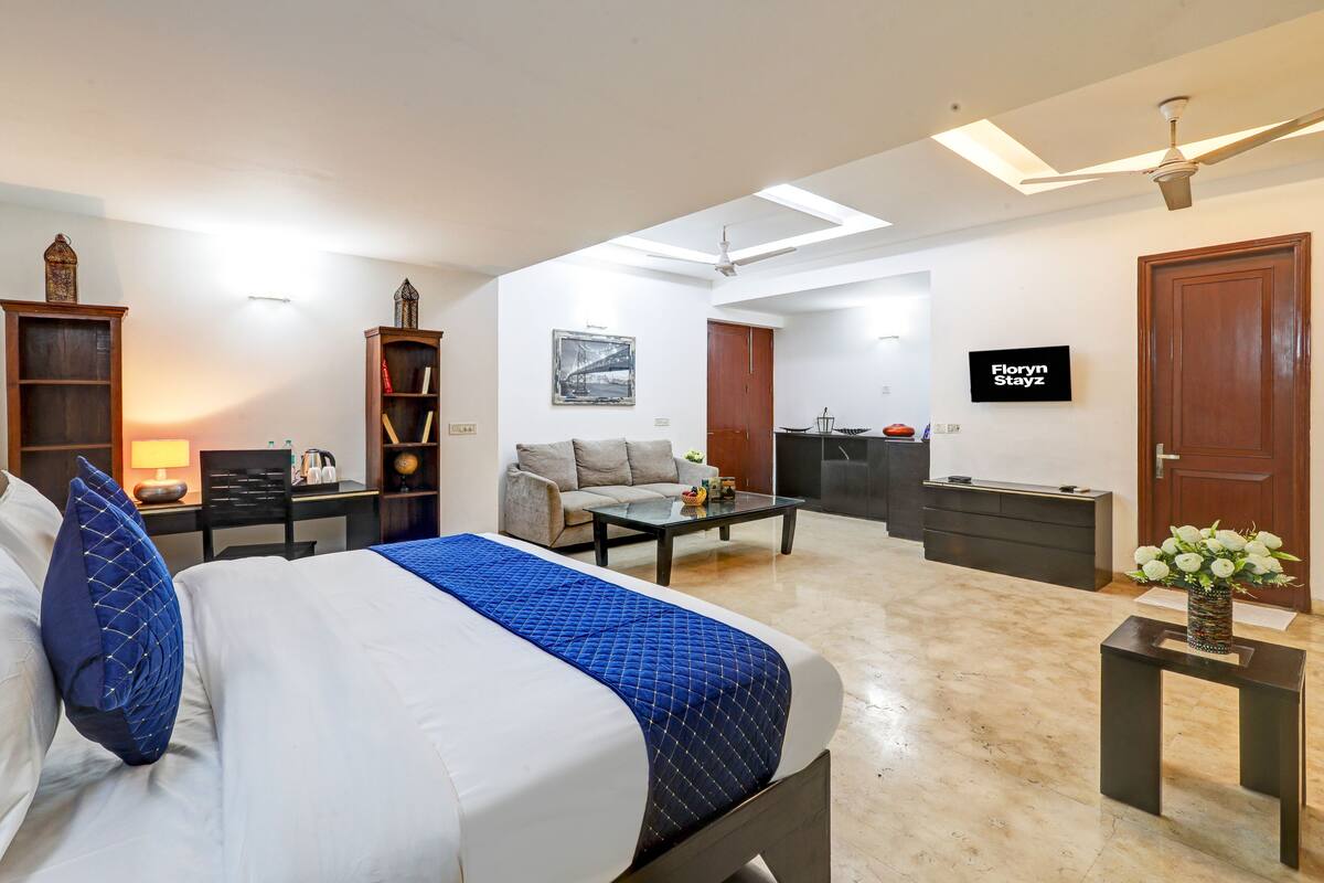 Une chambre d’hôtel avec un lit, un bureau, un canapé, une télévision et une petite table agrémentée de fleurs.