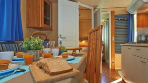 A cozy kitchen with wooden cabinets, a dining table set with breakfast items, and a view into the adjacent room. - Camping Rio Martino  (Latina)