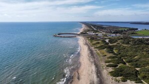 An aerial view of a coastal area with a sandy beach, a breakwater, and a mix of natural and developed land. - Camping Rio Martino  (Latina)