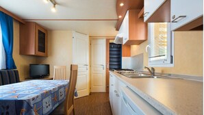 A compact kitchen with a dining area, a television, and a window with blinds. - Camping Rio Martino  (Latina)