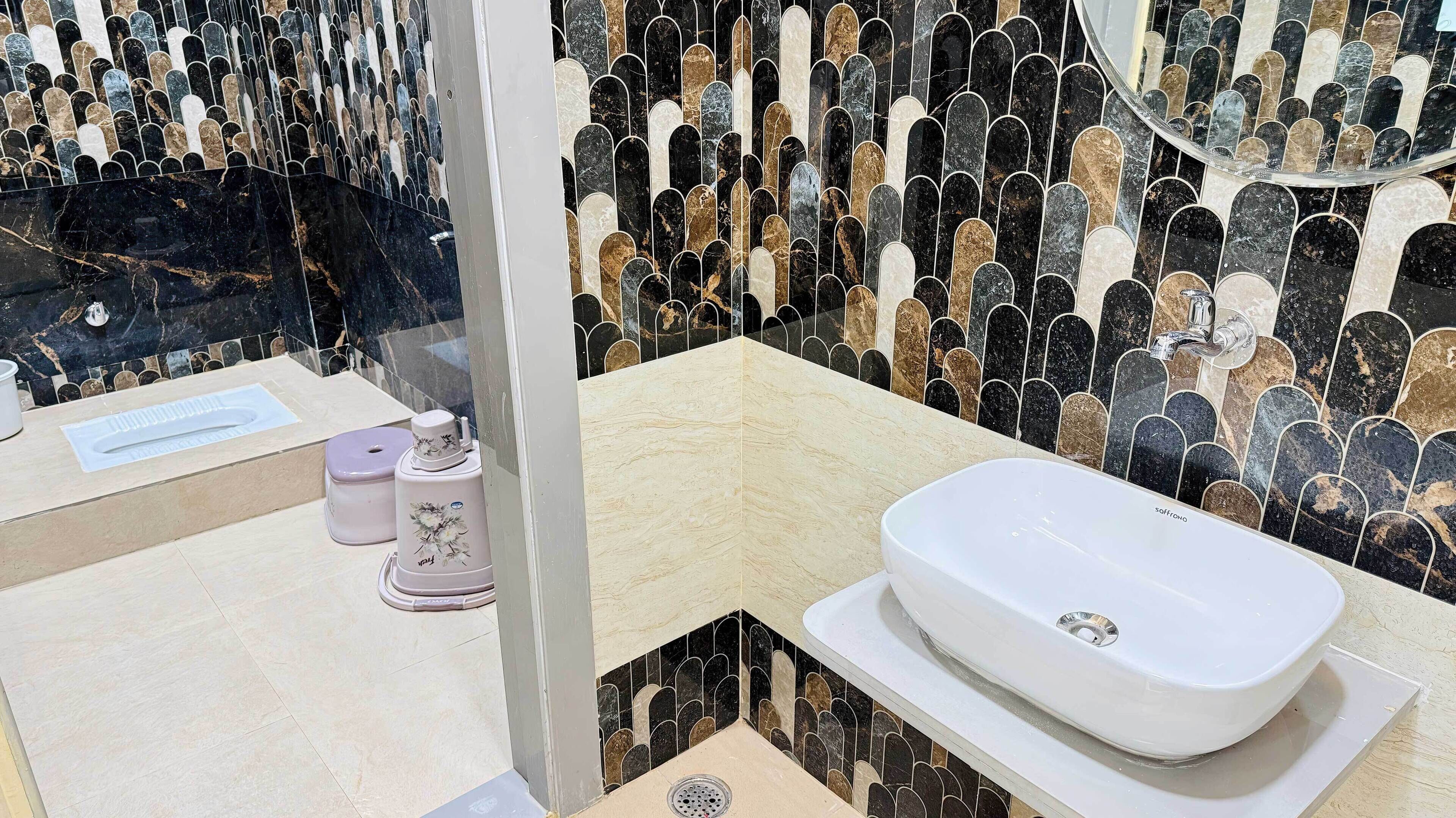 A modern bathroom with a white freestanding sink, a toilet, and a bidet. The walls are tiled with a black and gold pattern.