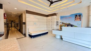 A reception area with a sofa, a reception desk, and a wall with a religious mural. - Hotel Om Mangalam Palace (Khandwa)