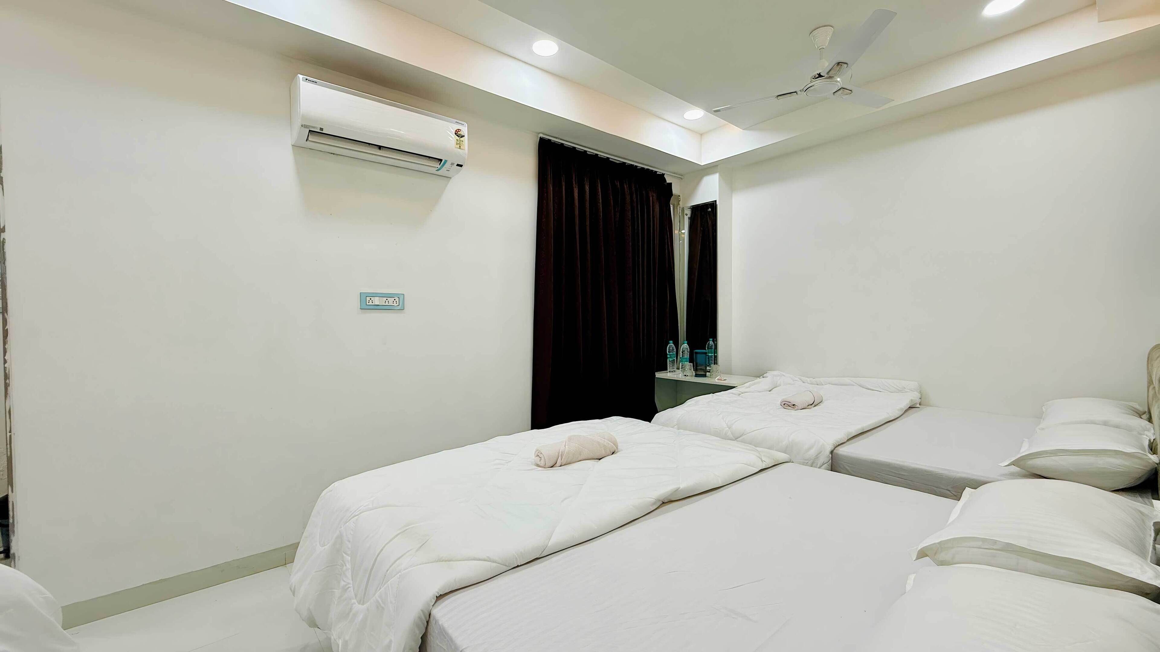 Habitación de hotel con dos camas, un equipo de aire acondicionado, ventilador de techo y una mesita con artículos de tocador.