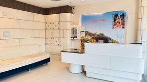 A reception area with a white reception desk, a bench, and a wall-mounted display. - Hotel Om Mangalam Palace (Khandwa)