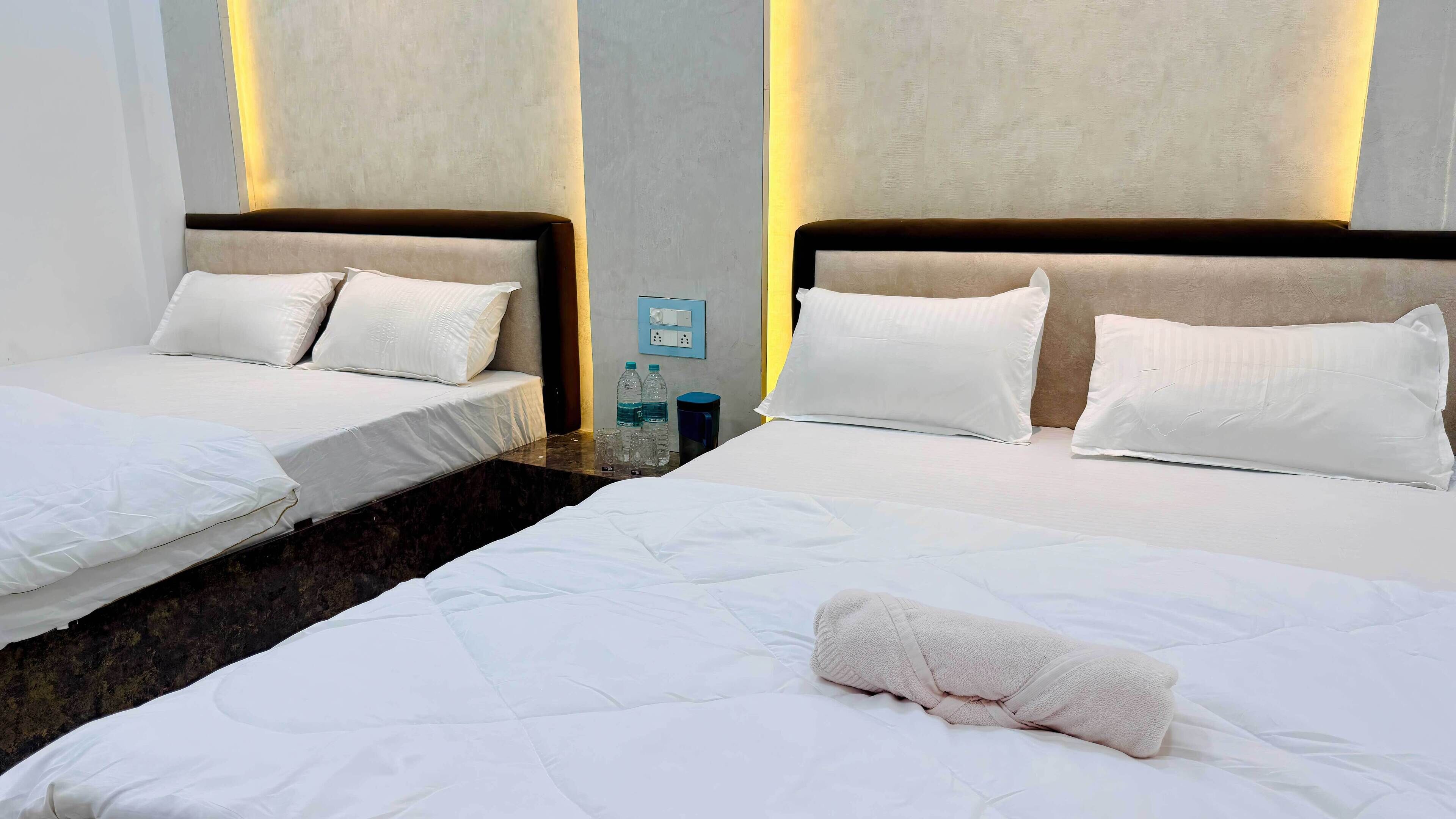 Dos camas individuales con ropa de cama blanca y cabeceros, una mesita con botellas de agua y un cubo de basura, y una toalla en el suelo.