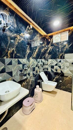 Un baño con pared de mármol, un salpicadero de azulejos geométricos, un lavamanos blanco, un inodoro y un bidé.