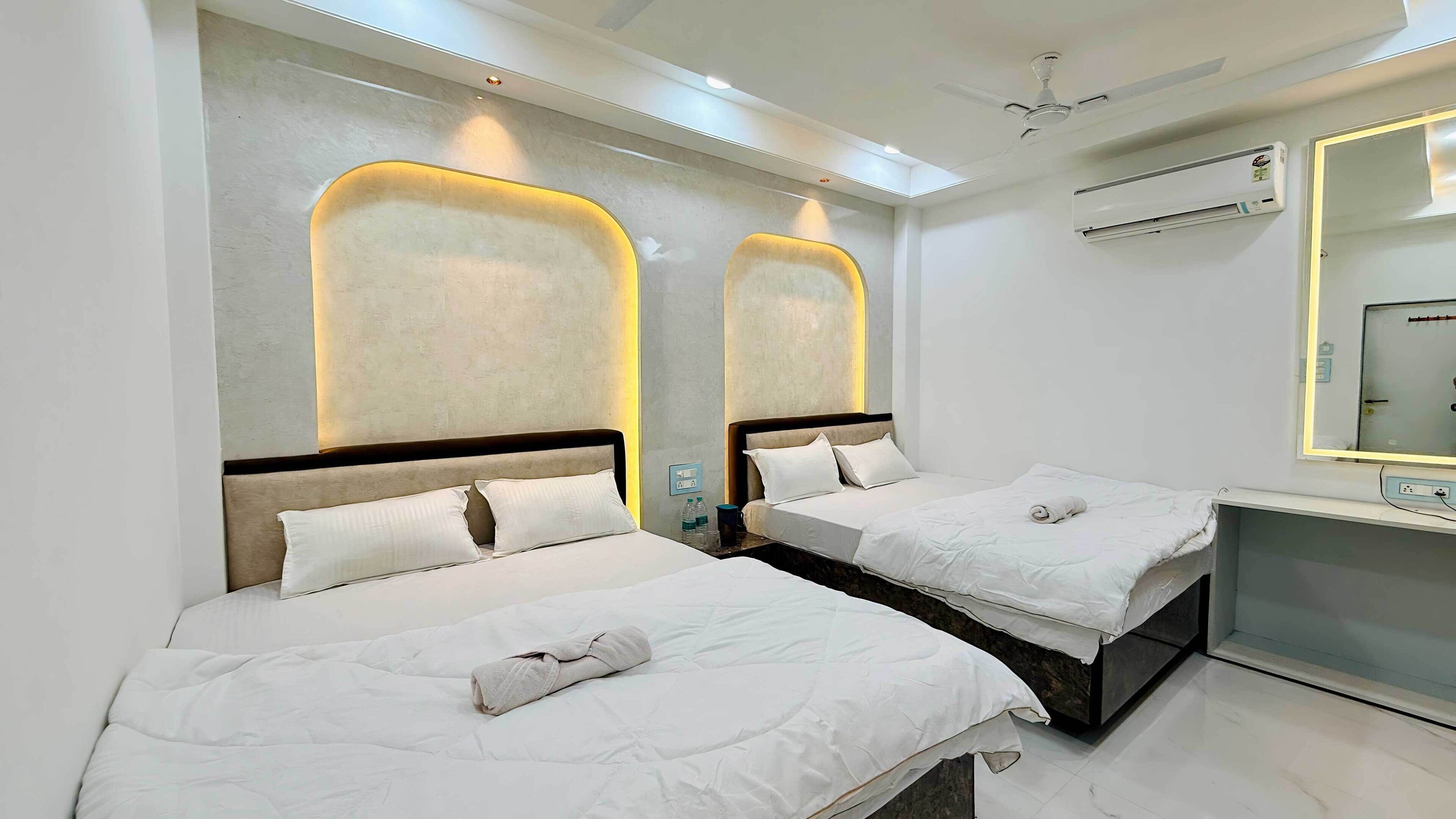 A hotel room with two beds, a desk, a mirror, and an air conditioning unit.