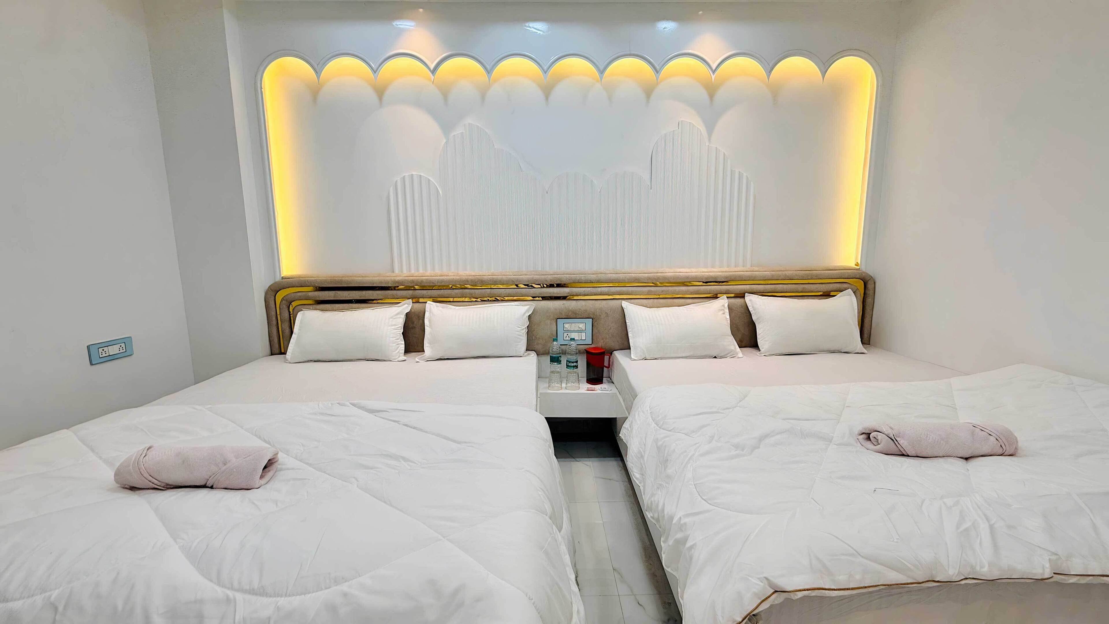 A hotel room with two beds, a nightstand, and a wall-mounted light fixture.