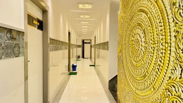 Un pasillo de hotel con suelo de baldosas, una puerta cerrada a la izquierda y una pared decorativa a la derecha.