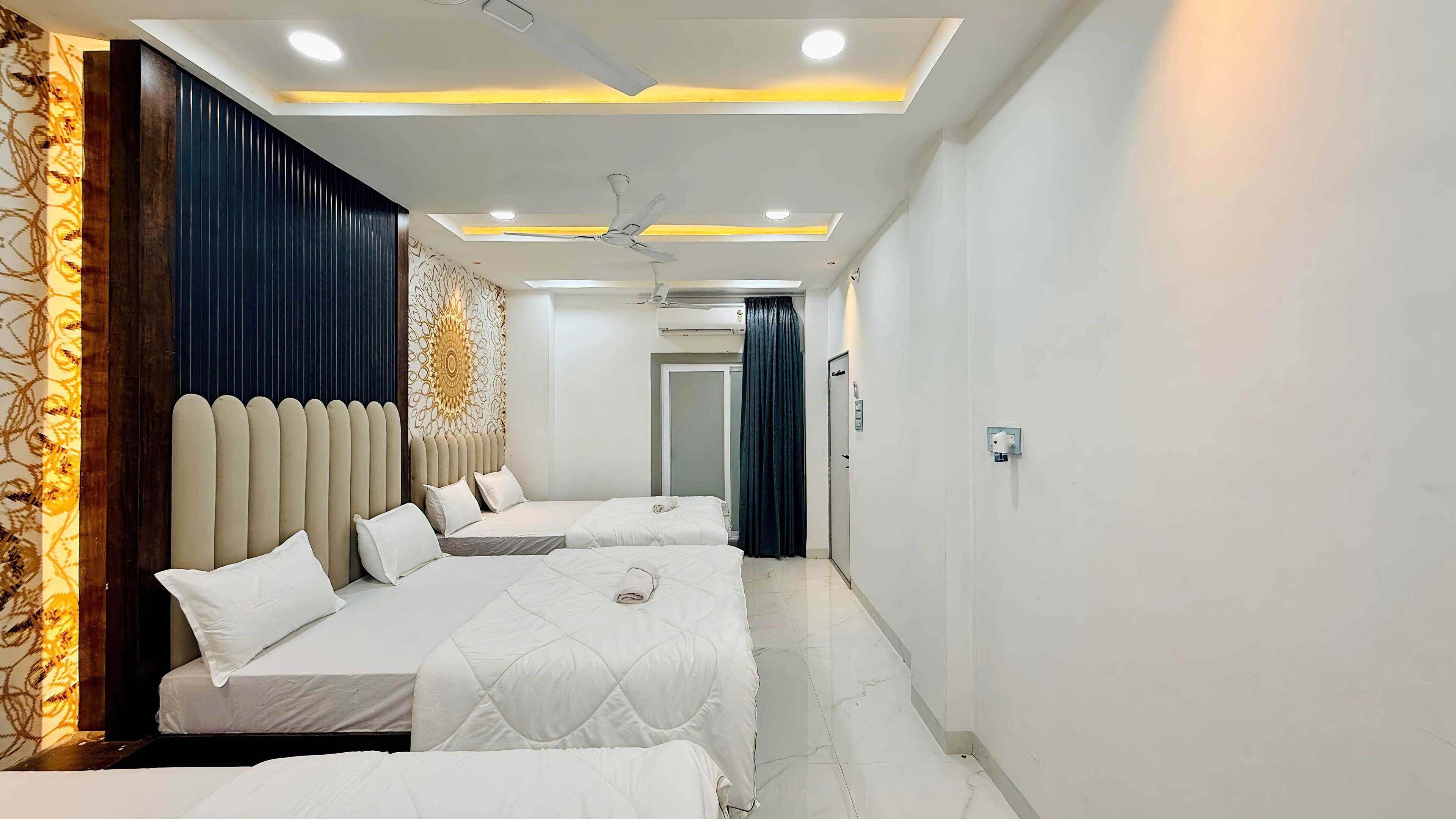 Ein Hotelzimmer mit drei nebeneinanderliegenden Betten, einem Deckenventilator, Einbauleuchten und einer Wand mit Muster auf der linken Seite.