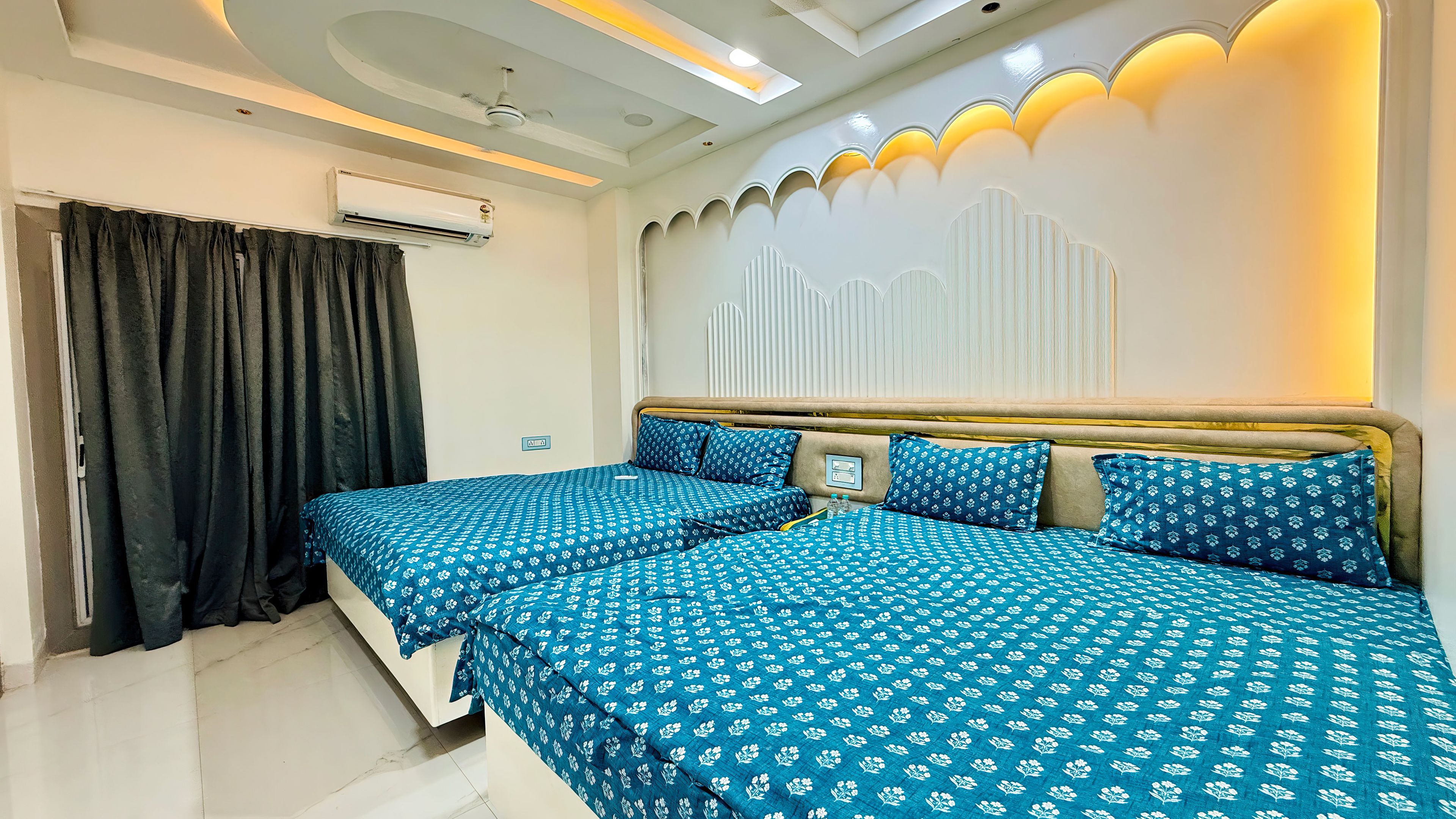 Habitación de hotel con cama, ventilador de techo, equipo de aire acondicionado y una pared con panel decorativo.