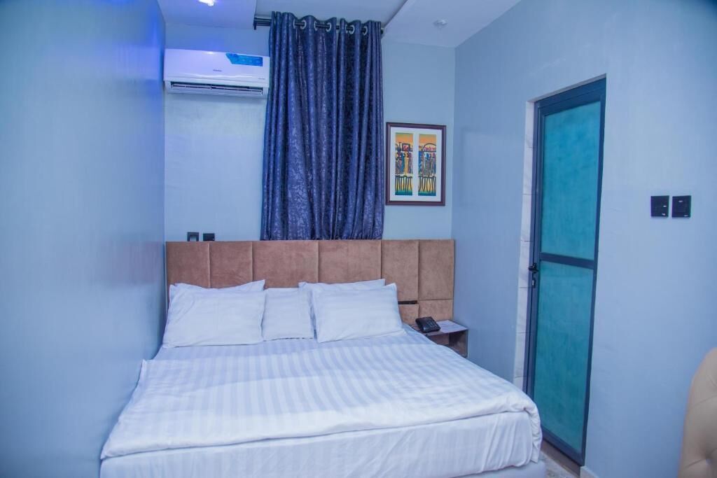 Habitación de hotel con cama, unidad de aire acondicionado, puerta y un cuadro en la pared.