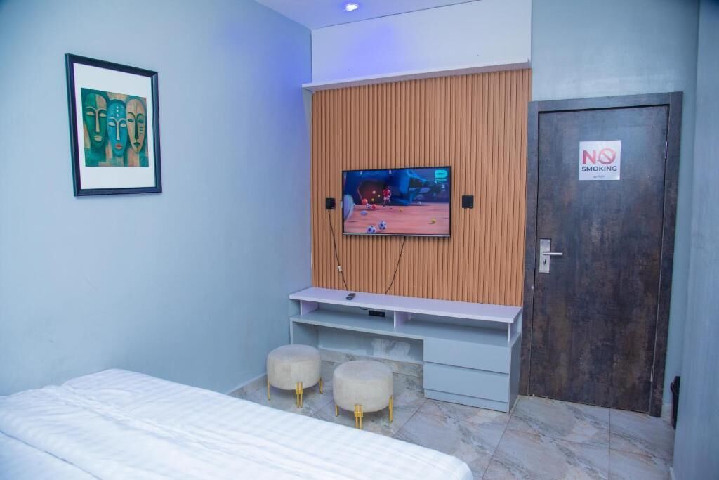 A hotel room with a bed, a TV mounted on a wooden panel wall, a 'No Smoking' sign, and a framed artwork on the wall.