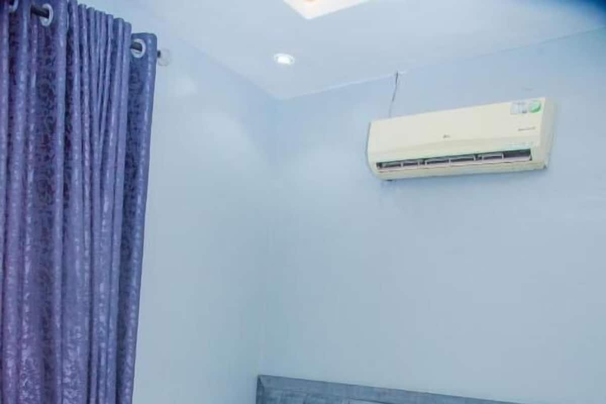 A bedroom with a bed, a headboard, a window, and an air conditioner.
