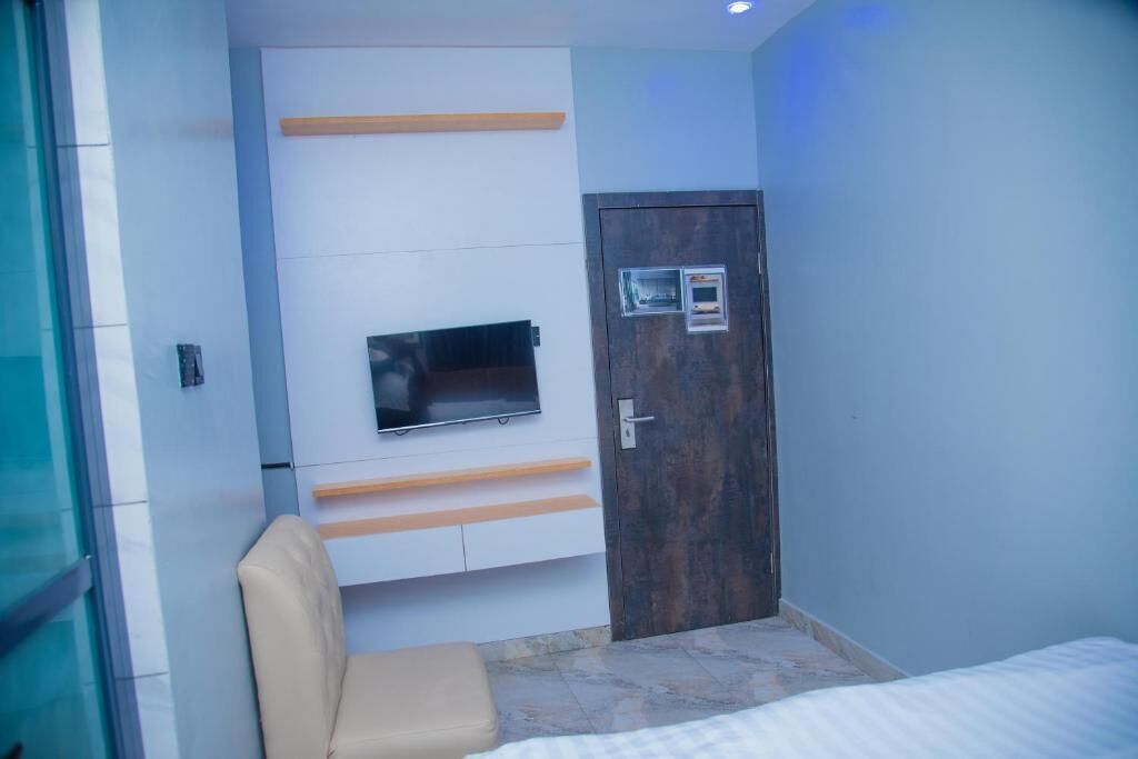 Una habitación moderna con una cama, un televisor montado en la pared, un estante de madera y una puerta con cerradura.