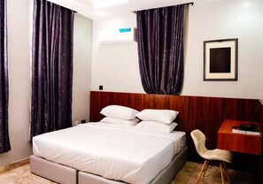 Habitación de hotel con cama, cabecero de madera, escritorio con silla y un cuadro en la pared.