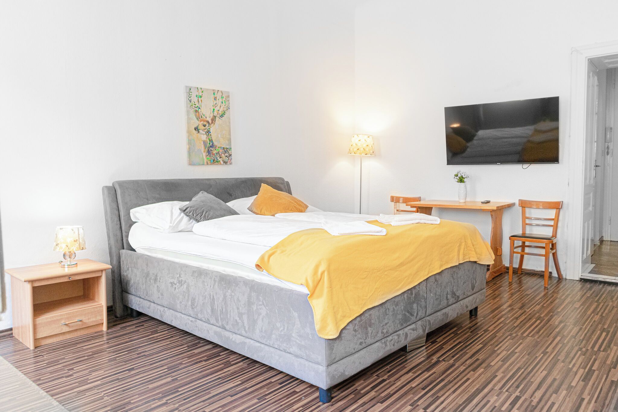 A modern bedroom with a bed, bedside tables, a desk, and a TV.