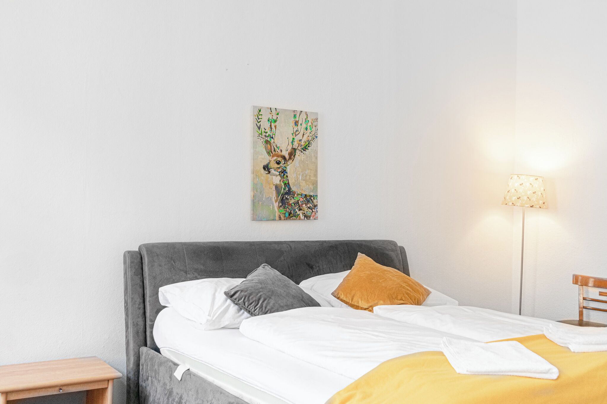 Un lit bien fait, avec du linge de lit blanc et jaune, une tête de lit grise et une petite table de chevet.
