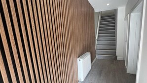 Ein Flur mit einer Wand aus Holzlatten, einem weißen Heizkörper und einer Treppe, die zu einer anderen Etage führt.