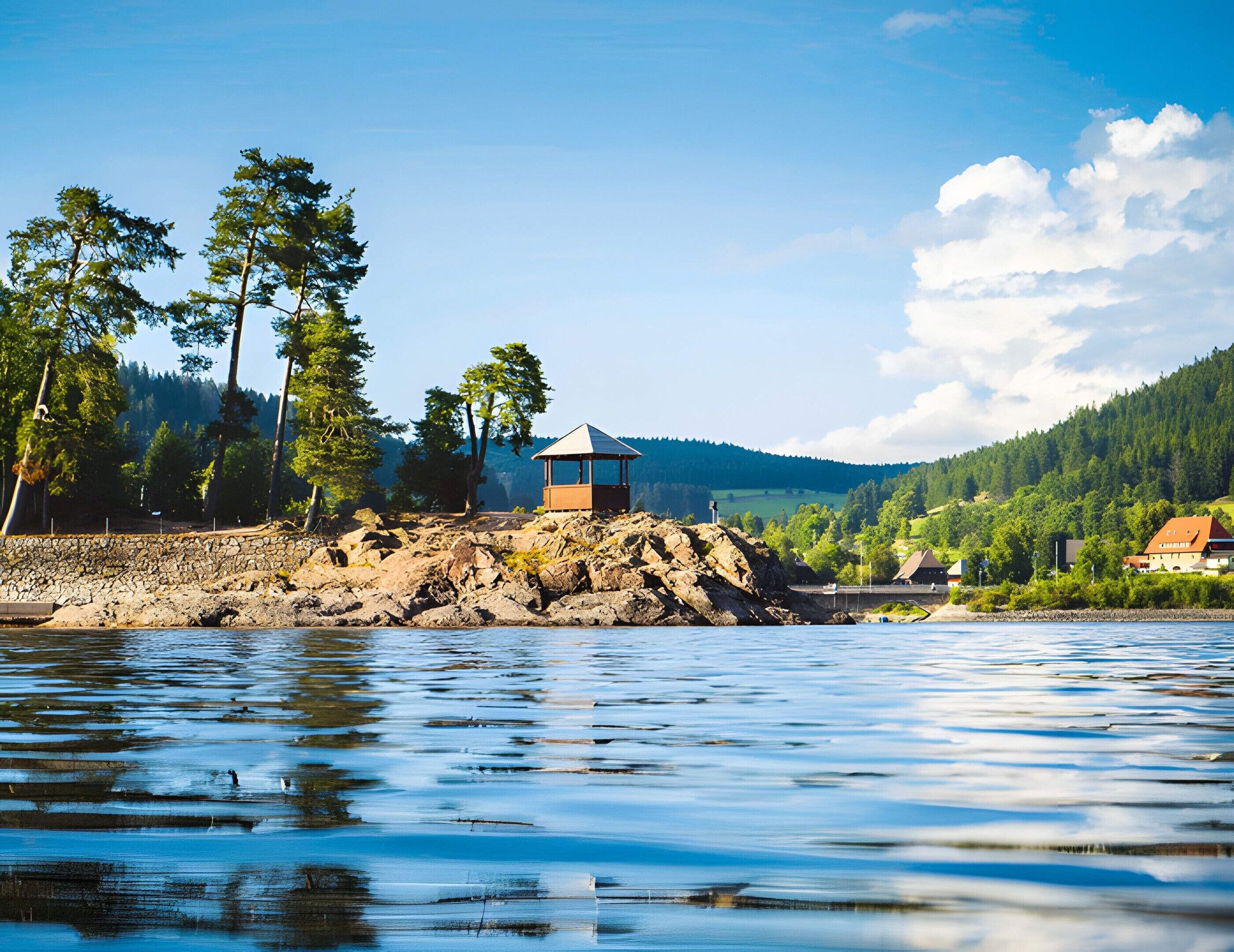 Blick auf einen See mit einem kleinen Holzbauwerk, umgeben von Bäumen und einer Steinmauer.