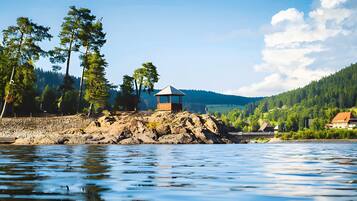 Blick auf einen See mit einem kleinen Holzbauwerk, umgeben von Bäumen und einer Steinmauer.