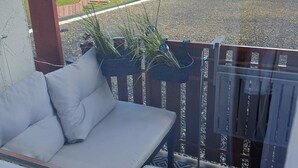 Un balcone con una divano, una pianta in vaso e un procione sull'unità di condizionamento.