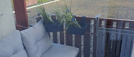 A balcony with a sofa, a potted plant, and a raccoon on the air conditioning unit.