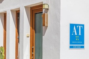 A building facade with three windows and a door, a blue sign with 'AT' and 'CIUDAD' indicating a city location. - 1 beach line. Malabau N4 (Tarifa)