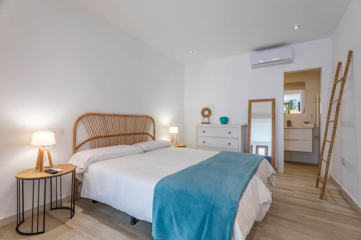 A bedroom with a bed, bedside tables, a dresser, an air conditioning unit, and a ladder.