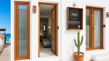 A hotel entrance with a sign for Malabau Beach House, a potted cactus, and a view of the beach.