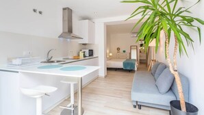 A modern kitchen with a white countertop, a sink, and a stove. There is a grey sofa and a large green plant in the living area. - 1 beach line. Malabau N6 (Tarifa)