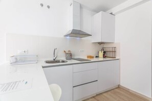 Cuina moderna amb armaris blancs, una aixeta d'acer inoxidable i una campana extractora.